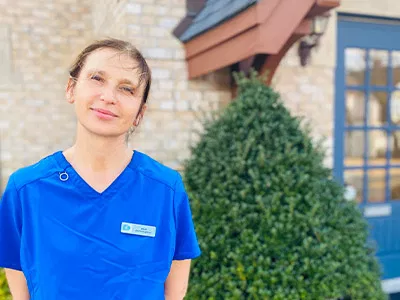 Female dental professional in blue scrubs standing outside modern dental office building.