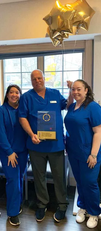 Three dental staff members in blue scrubs pose together in a modern dental office under holiday decoration.