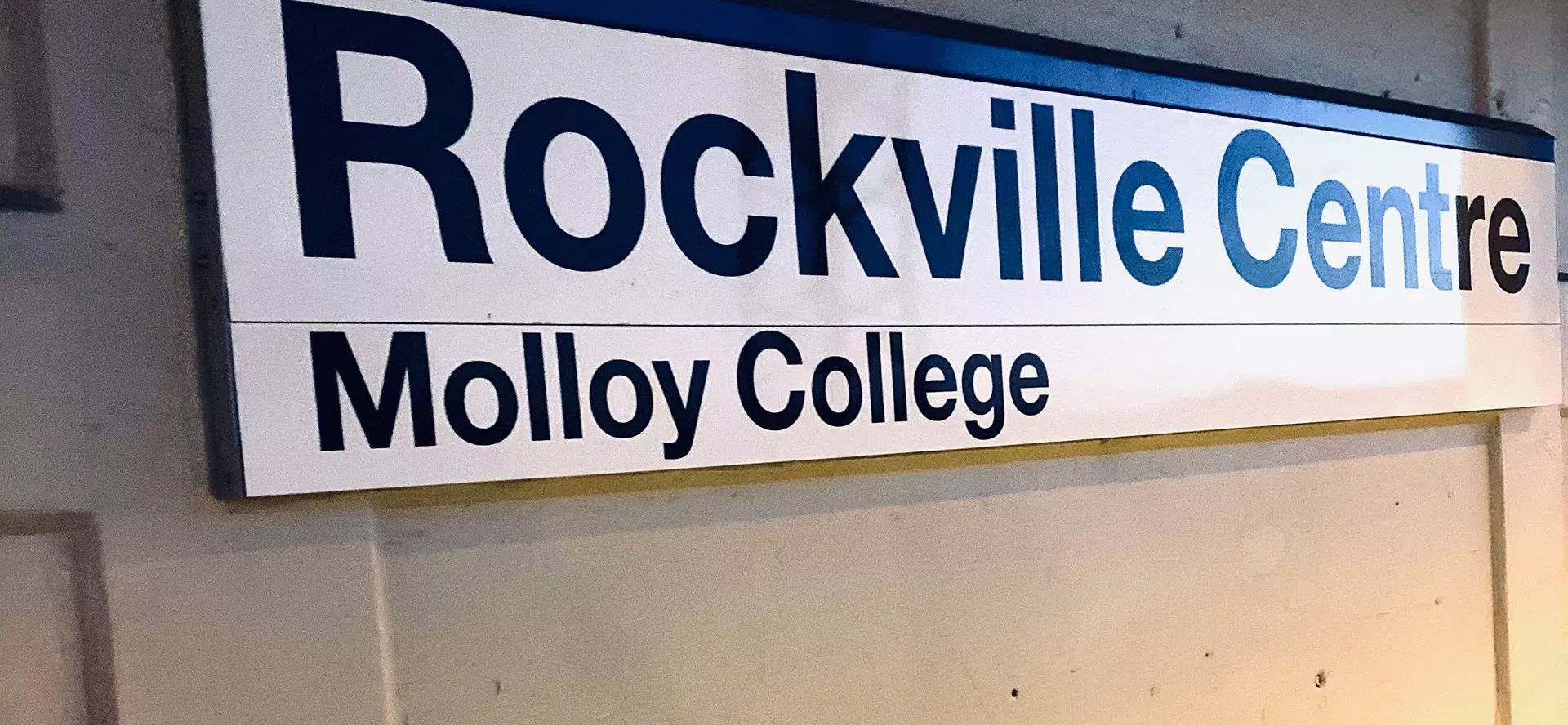 Illuminated sign reading "Rockville Centre Molloy College" in indoor institutional setting.