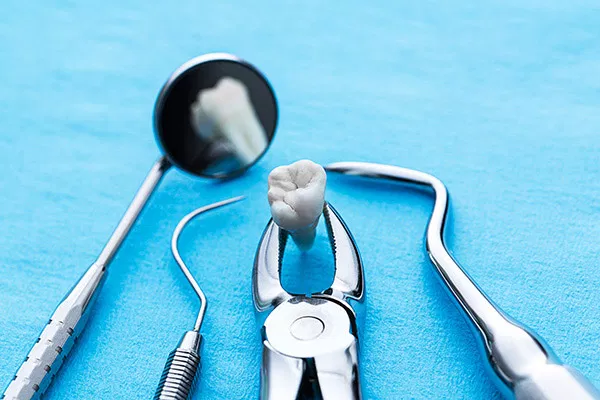 Dental instruments arranged on blue surface: mirror, forceps, and suction tool for professional dentistry.