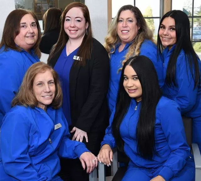 Team of six dental professionals in blue scrubs posing together in modern office setting.
