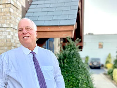 Professional man in blue shirt and tie standing outside dental office building.