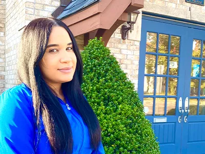 Young woman in blue shirt smiling outside blue door with ivy vines.