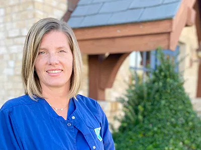 Woman in blue scrubs smiling outdoors in front of dental office building