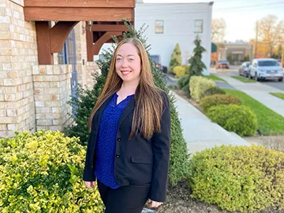 Professional woman smiling outside brick building with landscaping, dental office setting.