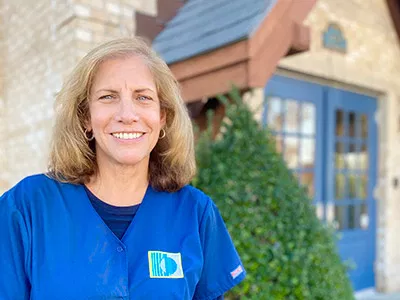 Smiling dental professional in blue scrubs standing outside modern dental office building