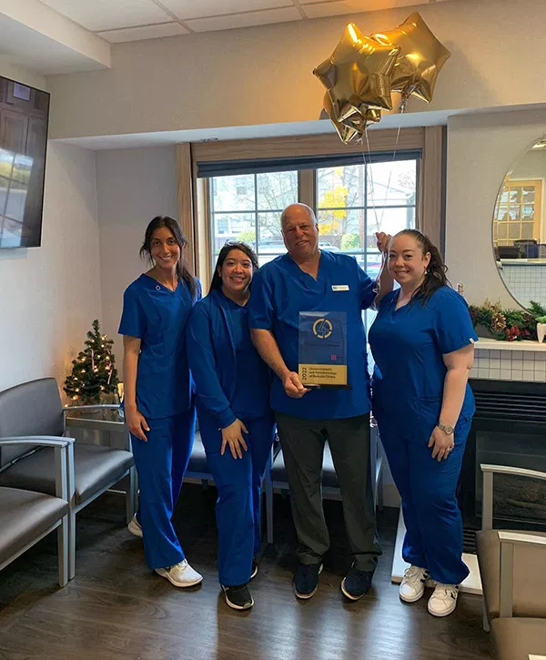 Four dental staff members in blue scrubs pose together in modern dental office with holiday decorations.