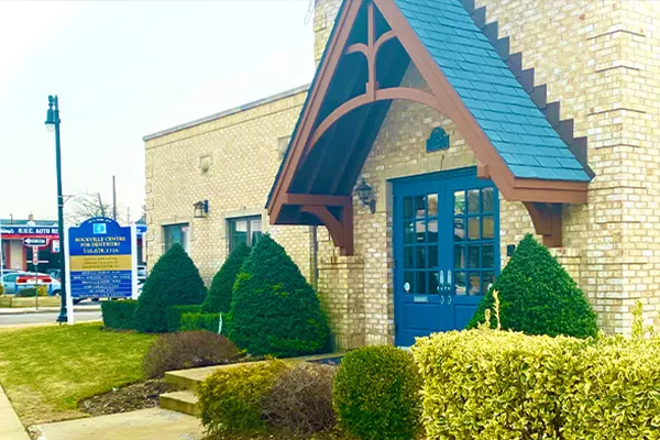 Rockville Centre for Dentistry exterior with blue door, brick facade, and manicured landscaping.