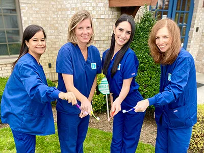 Four dental professionals in blue scrubs planting a tree together outdoors.