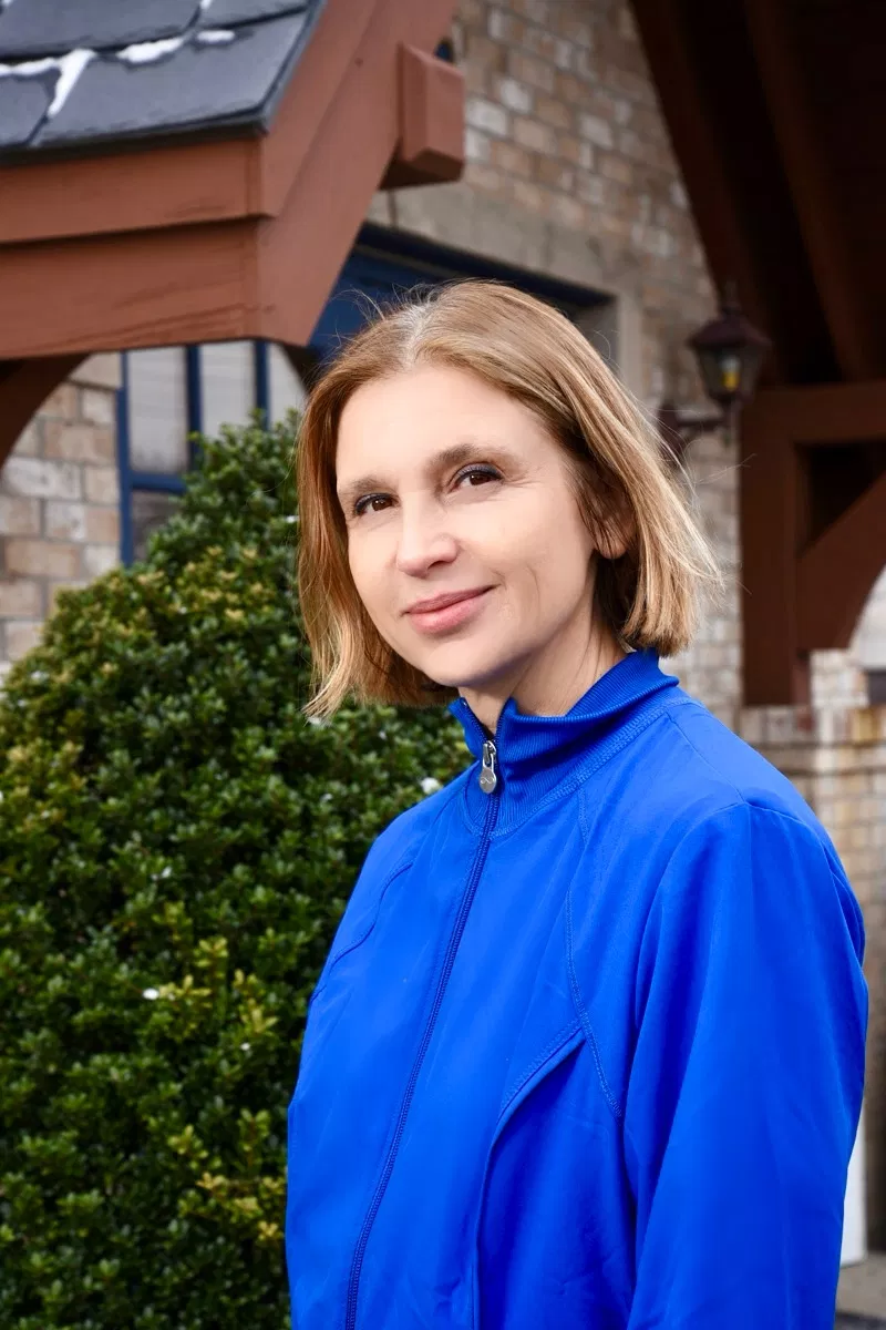Woman in blue jacket smiling outdoors in front of brick building with ivy.