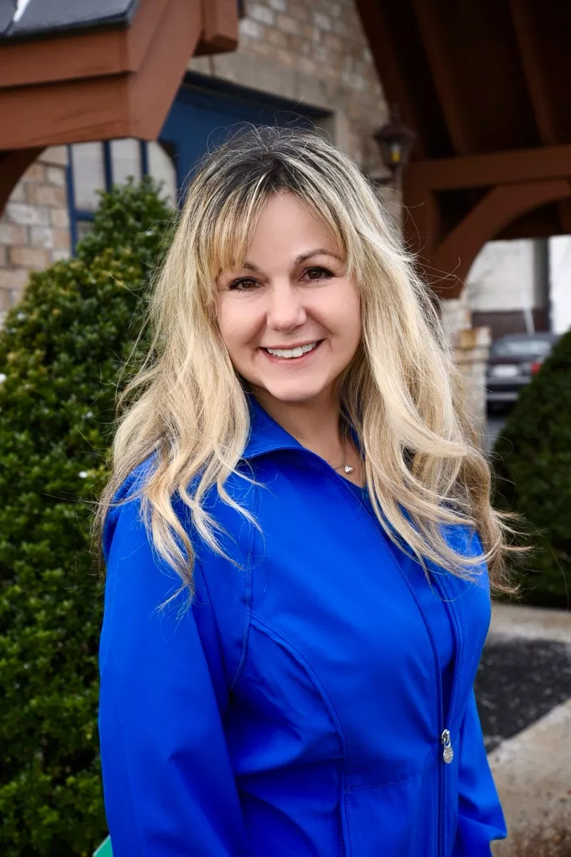 Woman in blue blouse smiling at camera outside dental office building.