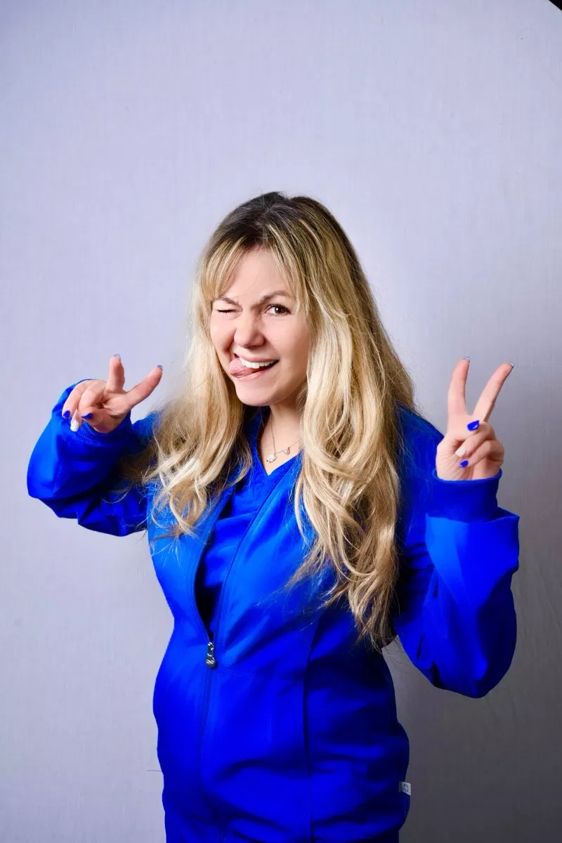 Woman in blue blazer making peace signs and smiling against neutral background