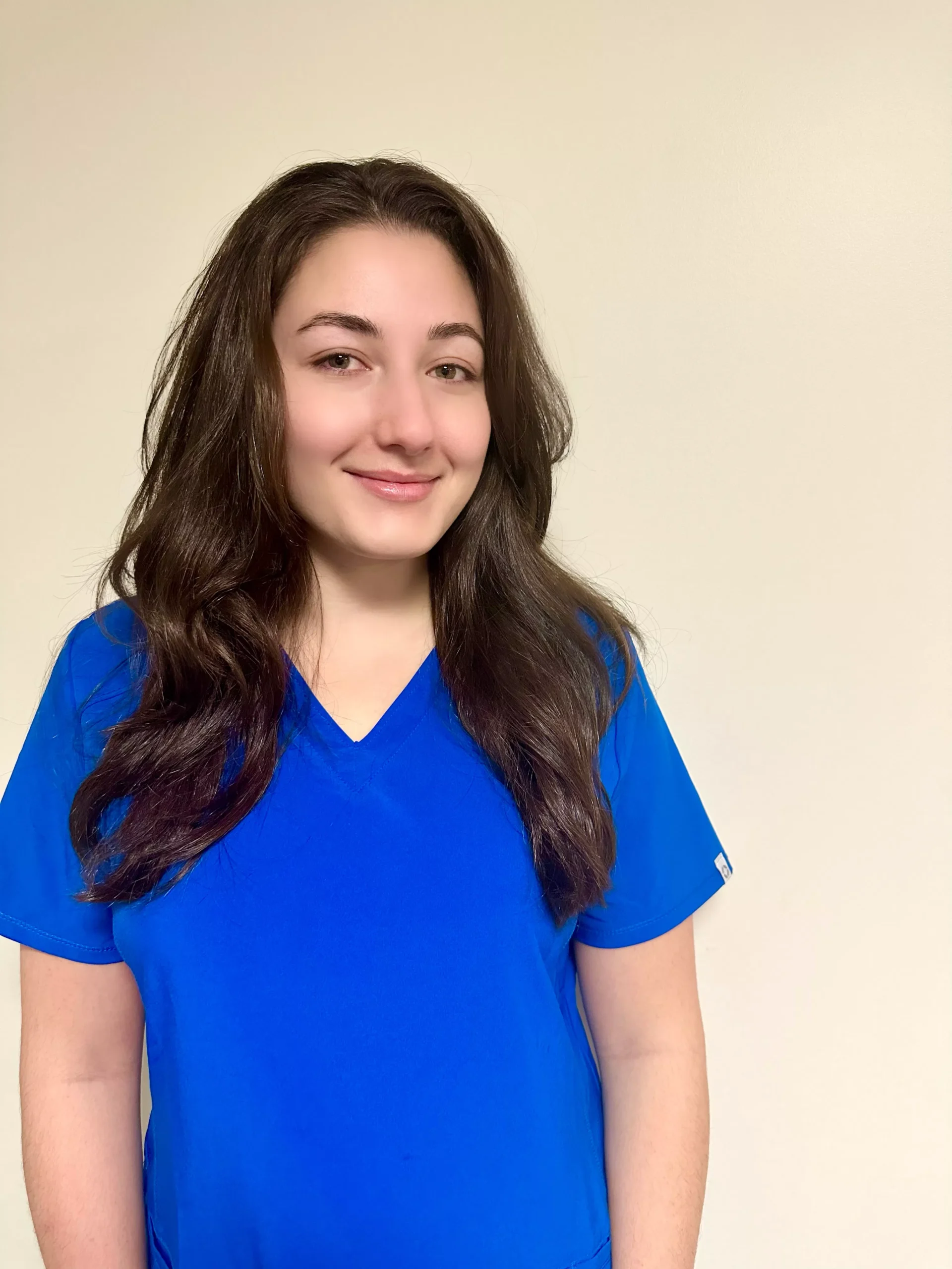 Young woman with long dark hair wearing blue v-neck shirt against neutral background.