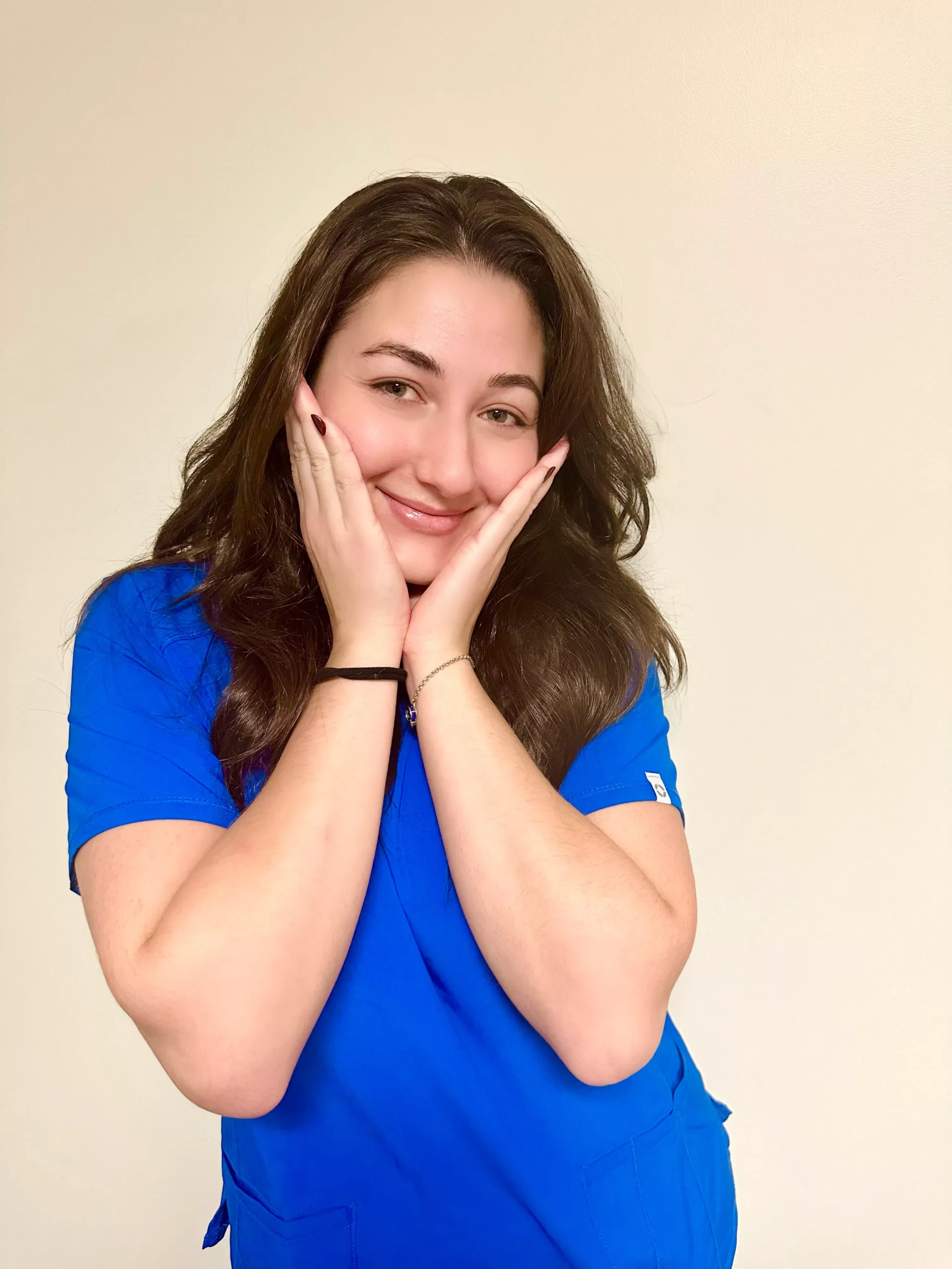 Smiling woman in blue shirt with hands to face against neutral background, professional headshot.