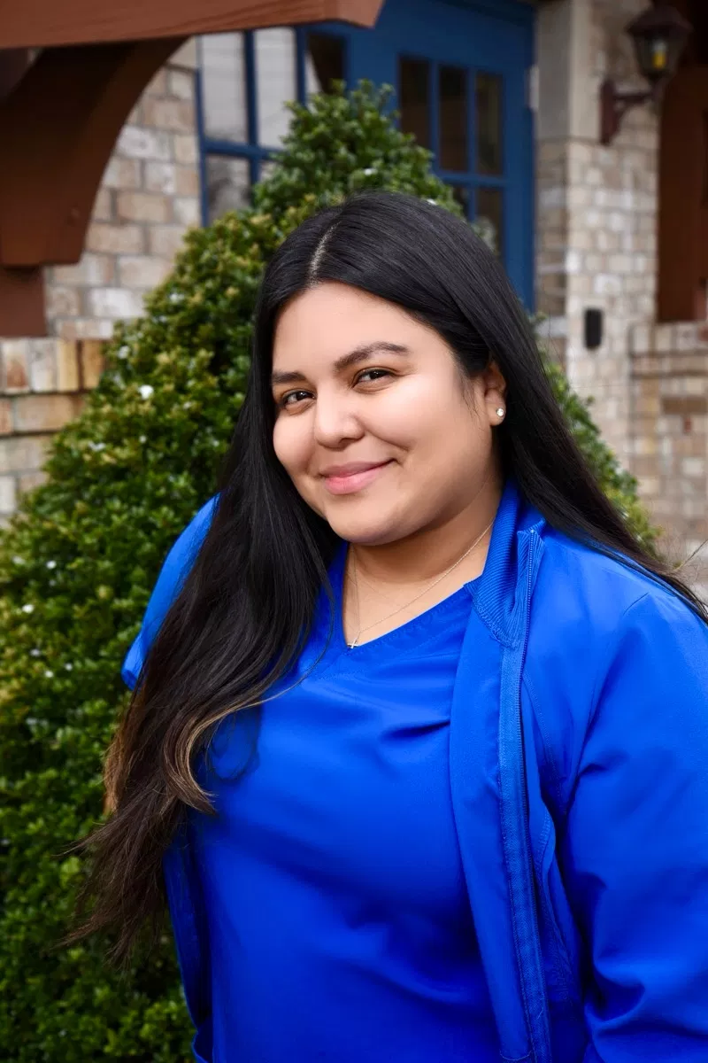 Woman in blue shirt smiling at camera against brick building with ivy.