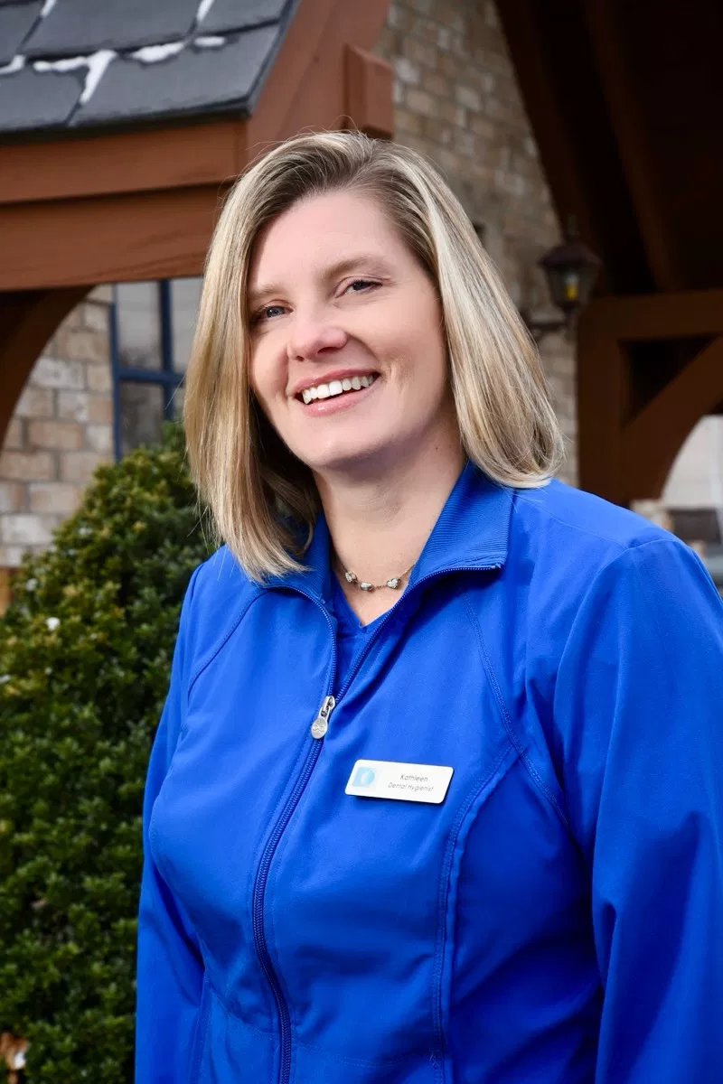 Professional woman in blue dental clinic uniform smiling outdoors at Rockville Centre for Dentistry.