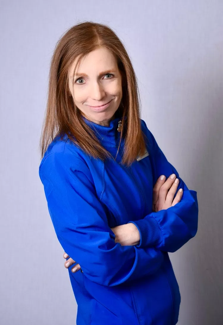 Professional woman in blue dental uniform with arms crossed against neutral background.