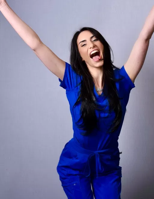 Woman in blue outfit with arms raised, smiling against gray background