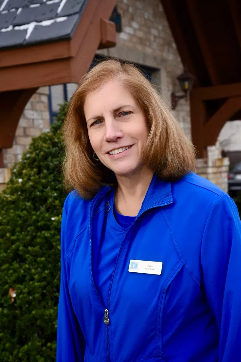 Professional woman in blue dental uniform smiling outdoors near clinic entrance.