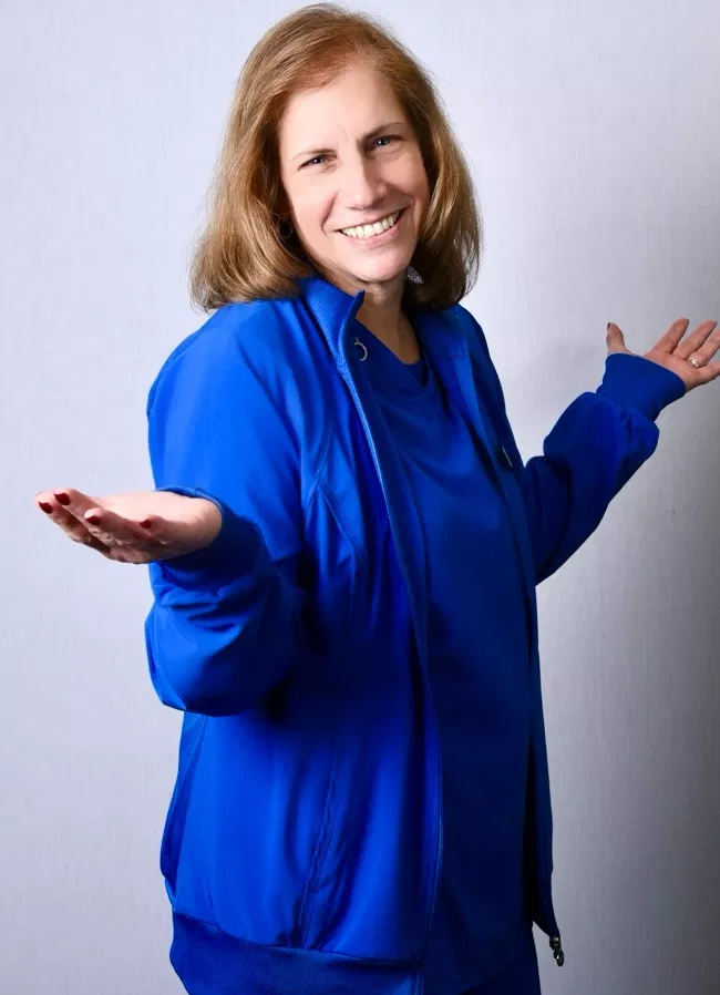Woman in blue jacket smiling with open arms against white background, professional portrait.