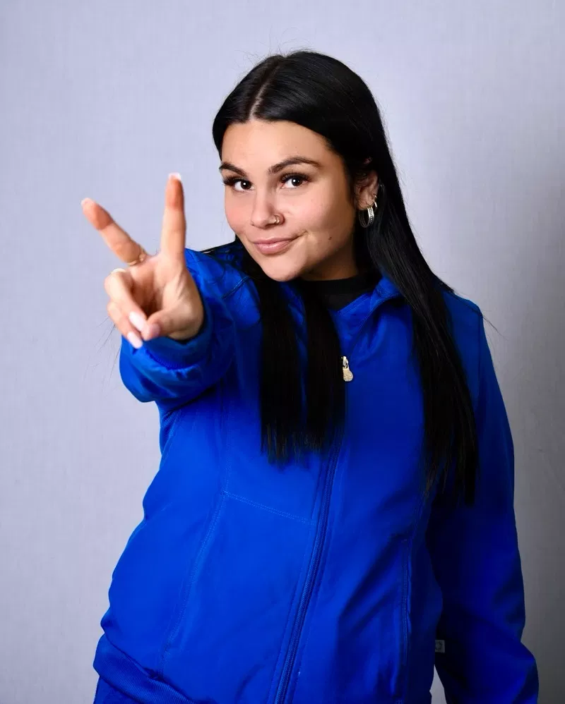 Woman in blue jacket making peace sign gesture against white background
