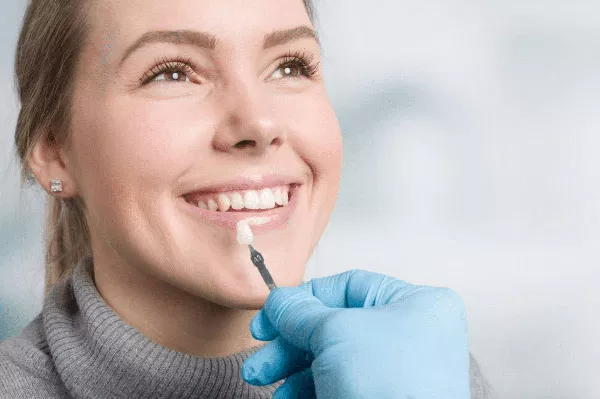 Woman smiling while dentist examines her teeth with blue gloved hands in clinical setting.