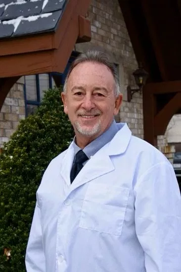 Professional dentist in white coat smiling outside dental office building