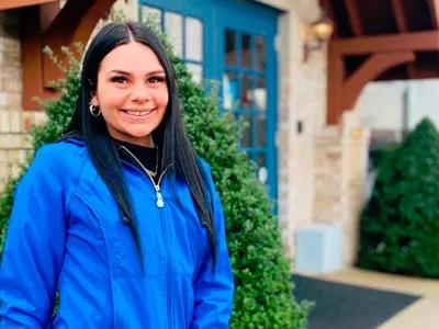 Woman in blue jacket smiling at camera outside dental office building with ivy.