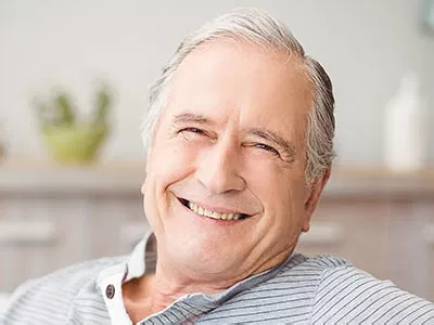 Smiling middle-aged man in striped shirt, dental office setting with blurred background.