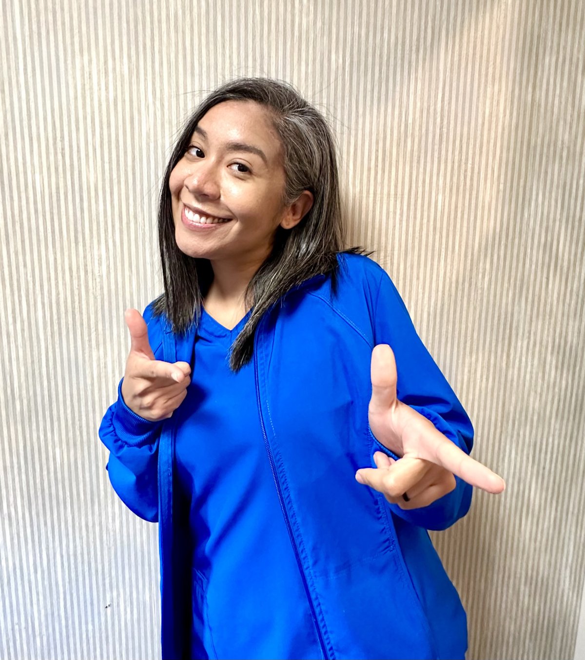Woman in blue jacket smiling and gesturing enthusiastically against textured beige background.