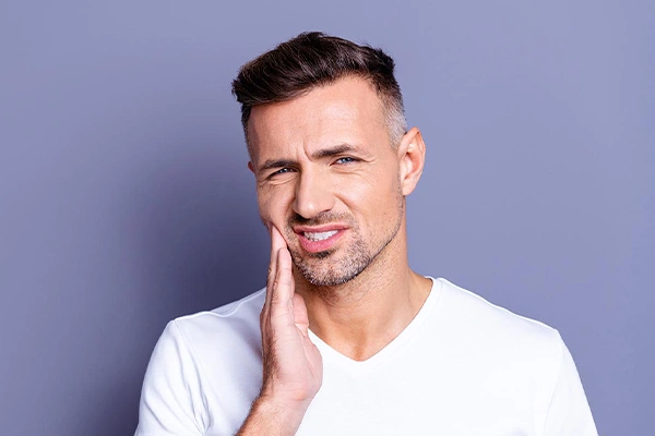 Man in white shirt smiling with hand to face against purple background, dental setting.