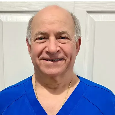 Male dentist in blue scrubs smiling at camera in clinical setting