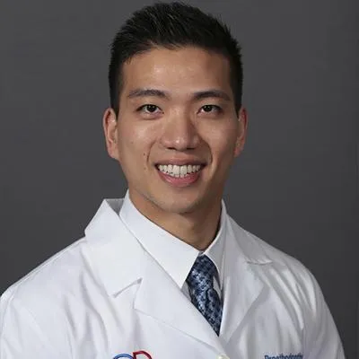 Male dentist in white coat and tie smiling at camera, professional headshot.