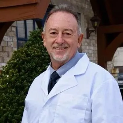 Male dentist in white coat smiling outside brick building with greenery