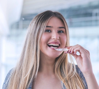 Young woman brushing teeth, smiling in bright dental office setting.