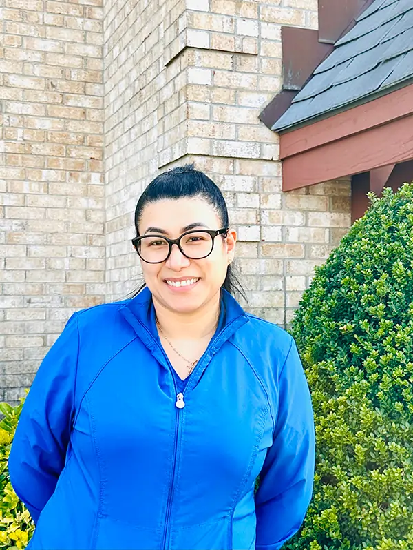 Woman in blue jacket and glasses smiling outside brick building with ivy.