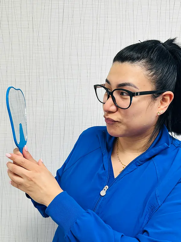Dental professional in blue scrubs examining dental mirror against white background.