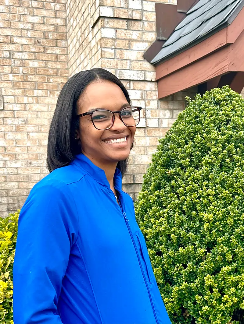 Woman in blue shirt smiling at camera outside brick building with ivy.