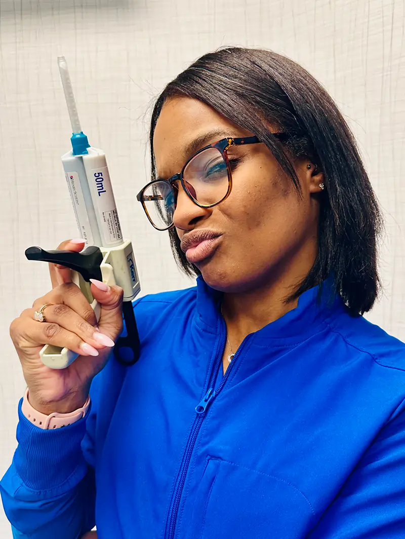 Female dentist in blue uniform holding dental tools against clinical white background.