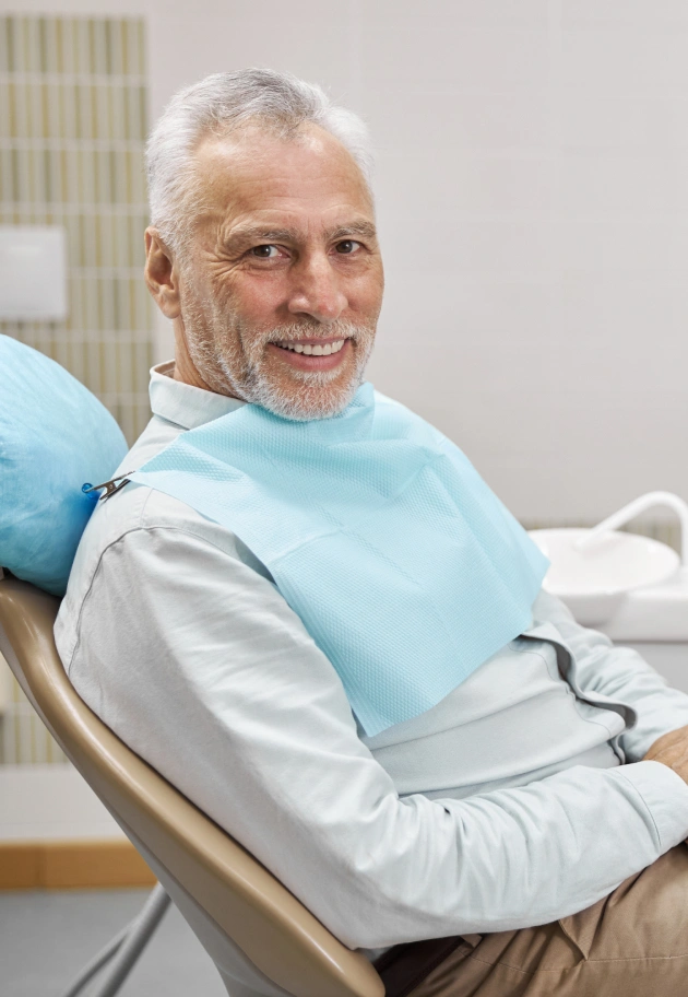 Senior man seated in dental chair wearing protective bib at dentistry office.