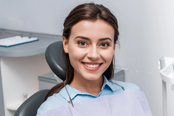 Smiling woman in dental chair wearing blue bib at modern dental office.