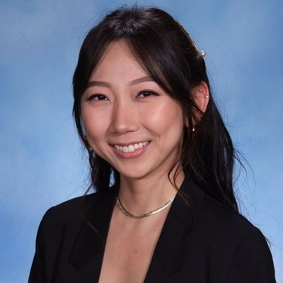 Professional headshot of smiling woman in black blazer against blue background