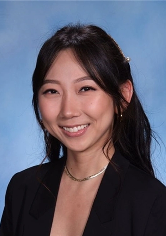 Professional headshot of a smiling woman in business attire against blue background.