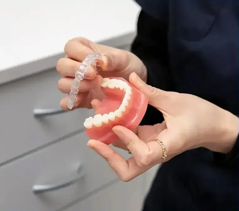 Dentist demonstrating dental prosthetic model showing teeth and gums in clinical setting.