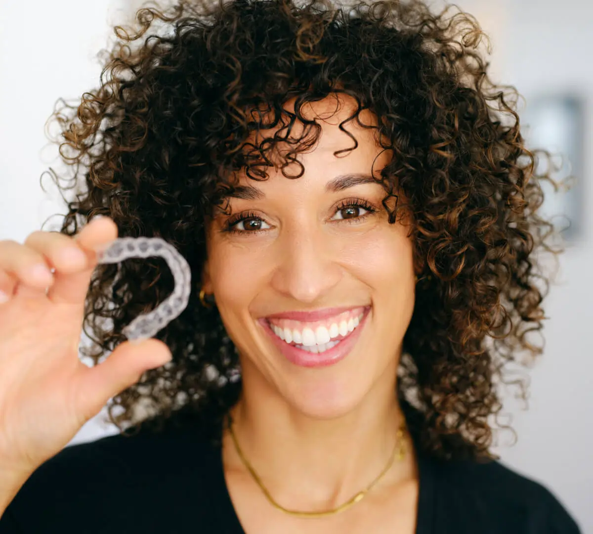 Smiling woman holding dental retainer in dental office setting.